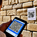 **

`A tourist uses a smartphone to scan a QR code at the Western Wall (Kotel) in Jerusalem. The app displays historical information and augmented reality overlays on the Wall, showing layers of history. In the background, other tourists are praying and observing the Wall. The scene is brightly lit, showcasing the ancient stones and modern technology integration.`

**